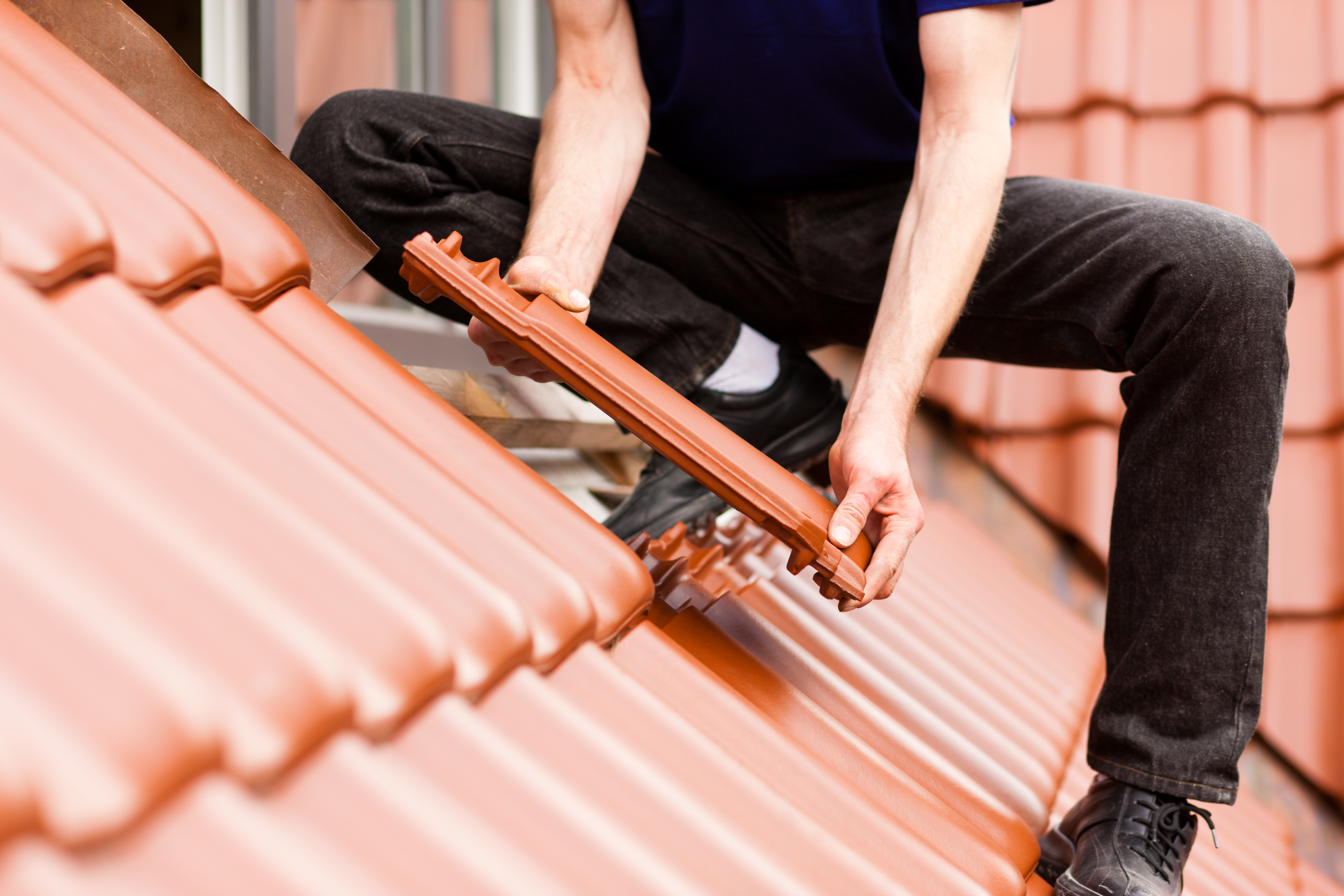 Roofing, construction worker standing on a roof covering it with tiles